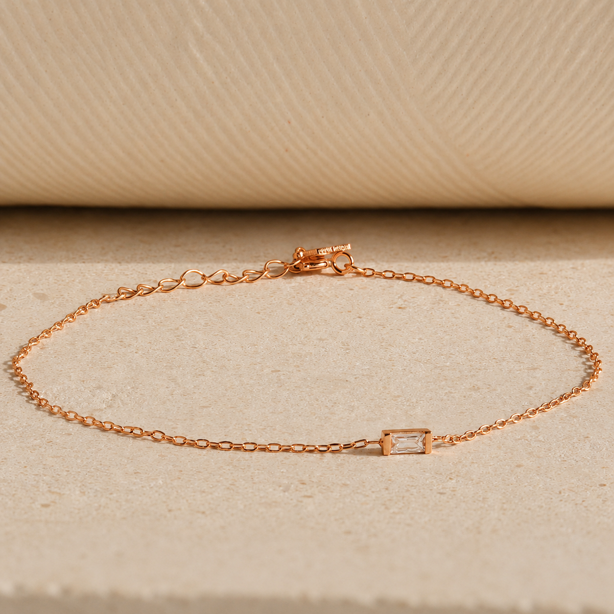 Rose gold bracelet with a small rectangular gemstone on a beige background